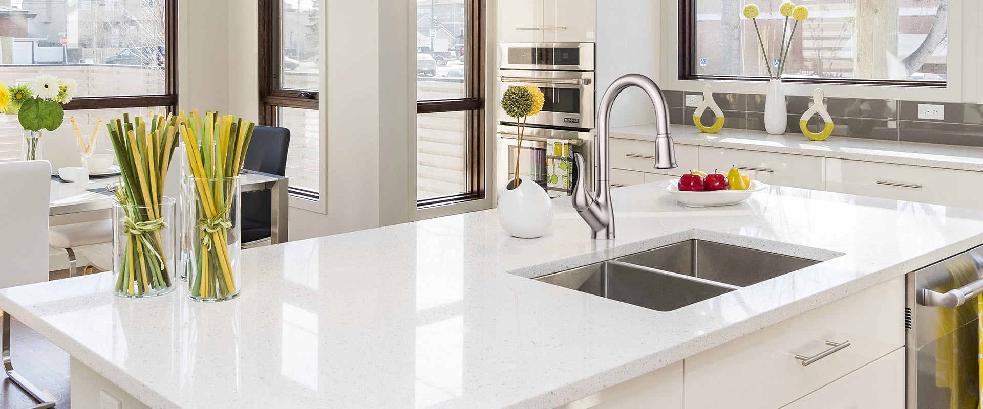 An elegant faucet is installed above a double bowl kitchen sink, complemented by attractive white granite marble.