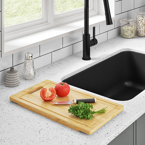 Slices of tomato and cilantro, alongside a knife on a bamboo cutting board, are placed beside an elegant black kitchen sink and faucet.