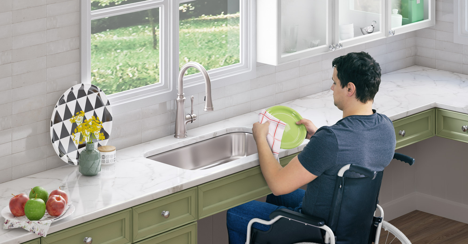 A young man in a wheelchair is washing dishes at an ADA-compliant kitchen sink.