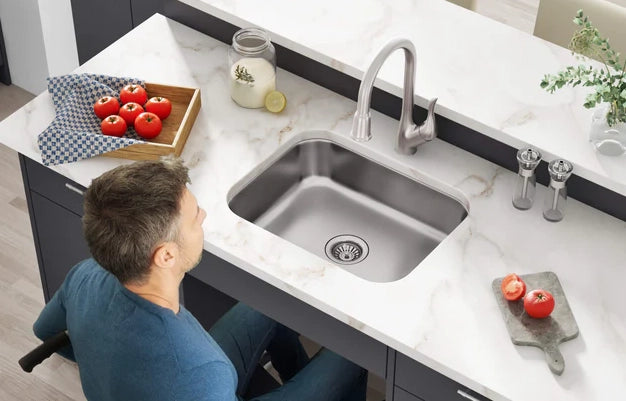 A man in a wheelchair is utilizing an ADA-compliant kitchen faucet and sink.